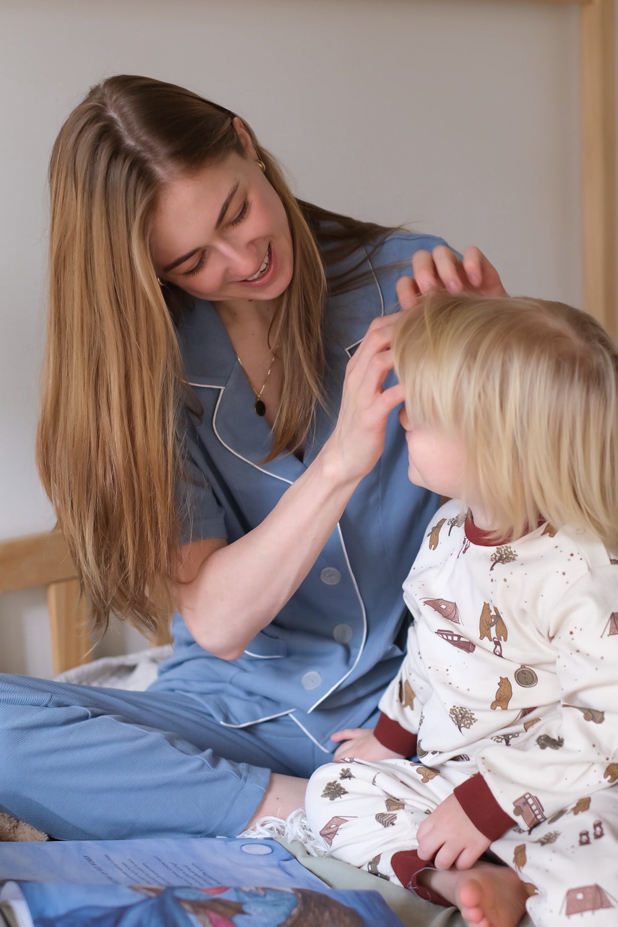 Woman and child in pajamas sitting on a bed with a book, smiling.