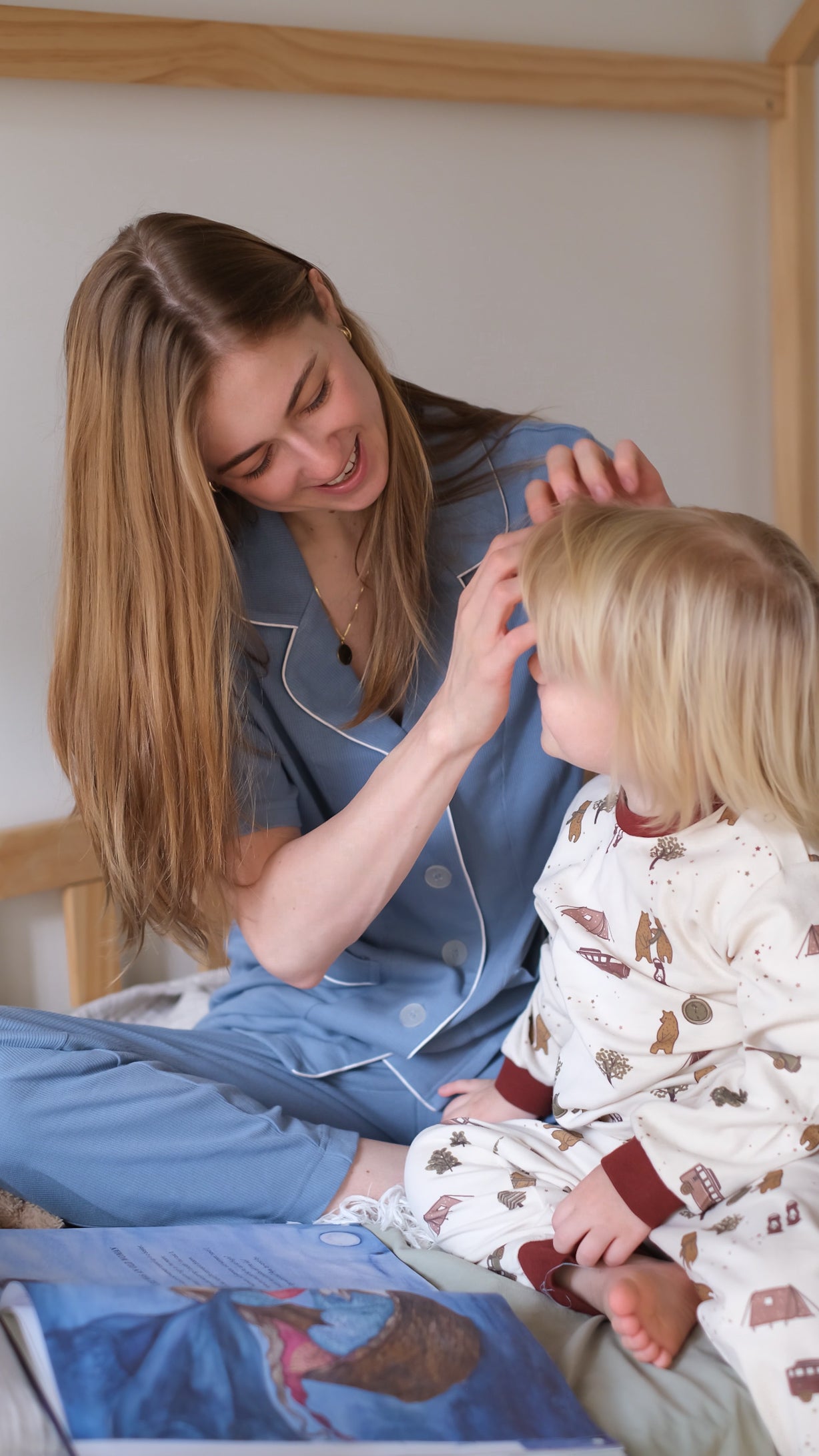 Woman and child in pajamas sitting on a bed with a book, smiling.