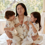 A woman and her two kids sit happily on a bed, all wearing soft summer pajamas, creating a warm family moment