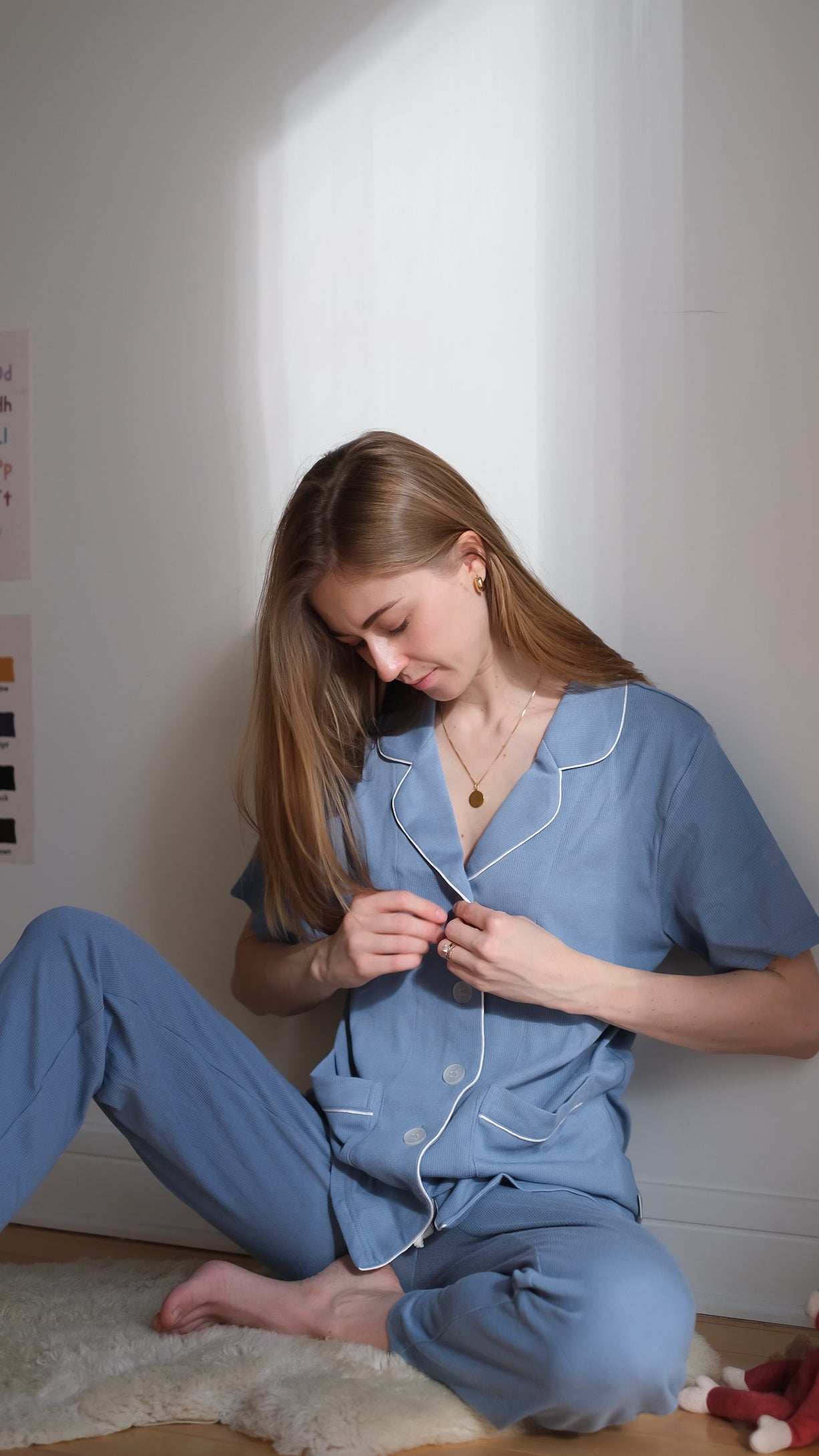 Woman in blue pajamas sitting on a rug in a softly lit room.