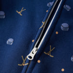 Close-up of a navy blue zippered garment with a repeating pattern of gold hockey sticks and white hockey helmets, showing the white zipper pull.