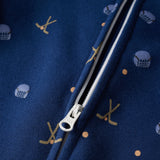 Close-up of a navy blue zippered garment with a repeating pattern of gold hockey sticks and white hockey helmets, showing the white zipper pull.