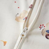Close-up of a cream-colored zippered garment with a soft pastel animal and berry print, featuring a white zipper pull with 'YKK' branding.