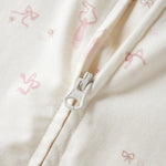 Close-up of a cream-colored fabric garment with a silver zipper and a subtle pink bow pattern.
