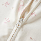 Close-up of a cream-colored fabric garment with a silver zipper and a subtle pink bow pattern.